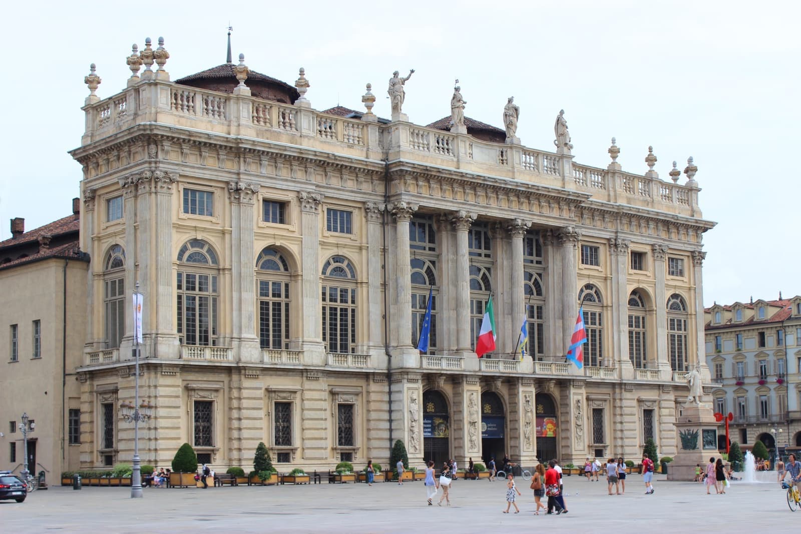 A pale baroque palace front with tall windows and statues along the roofline, on a wide square