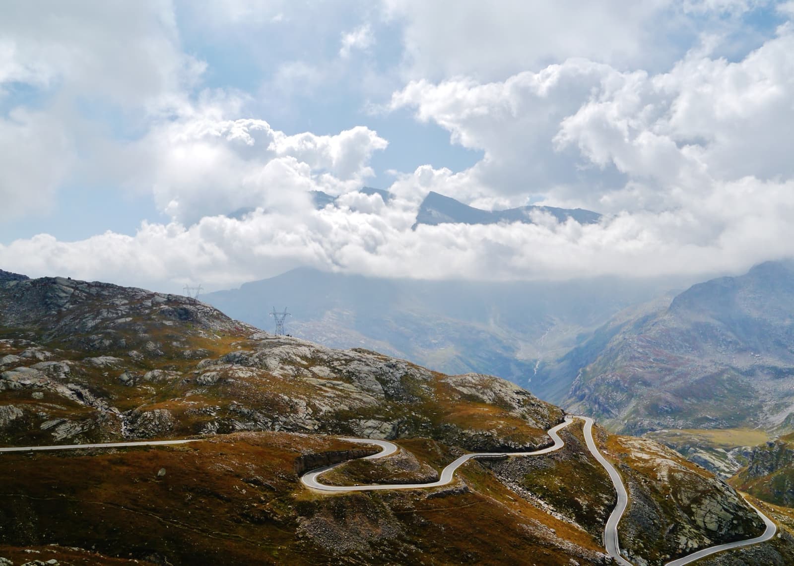 A narrow road zigzagging up a bare mountainside under a cloudy sky