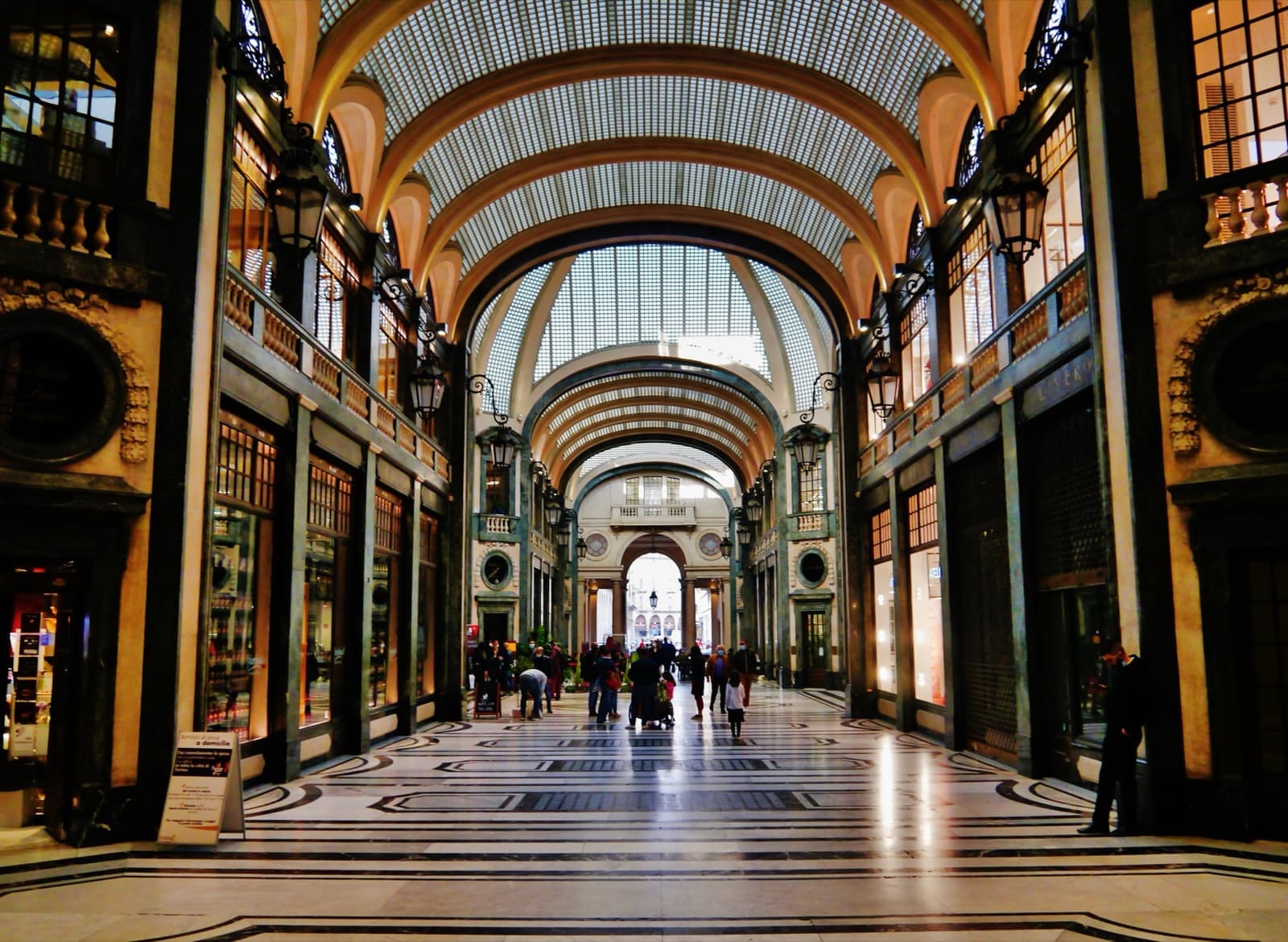 A tall arcade with a curved glass ceiling, polished floor and shop fronts