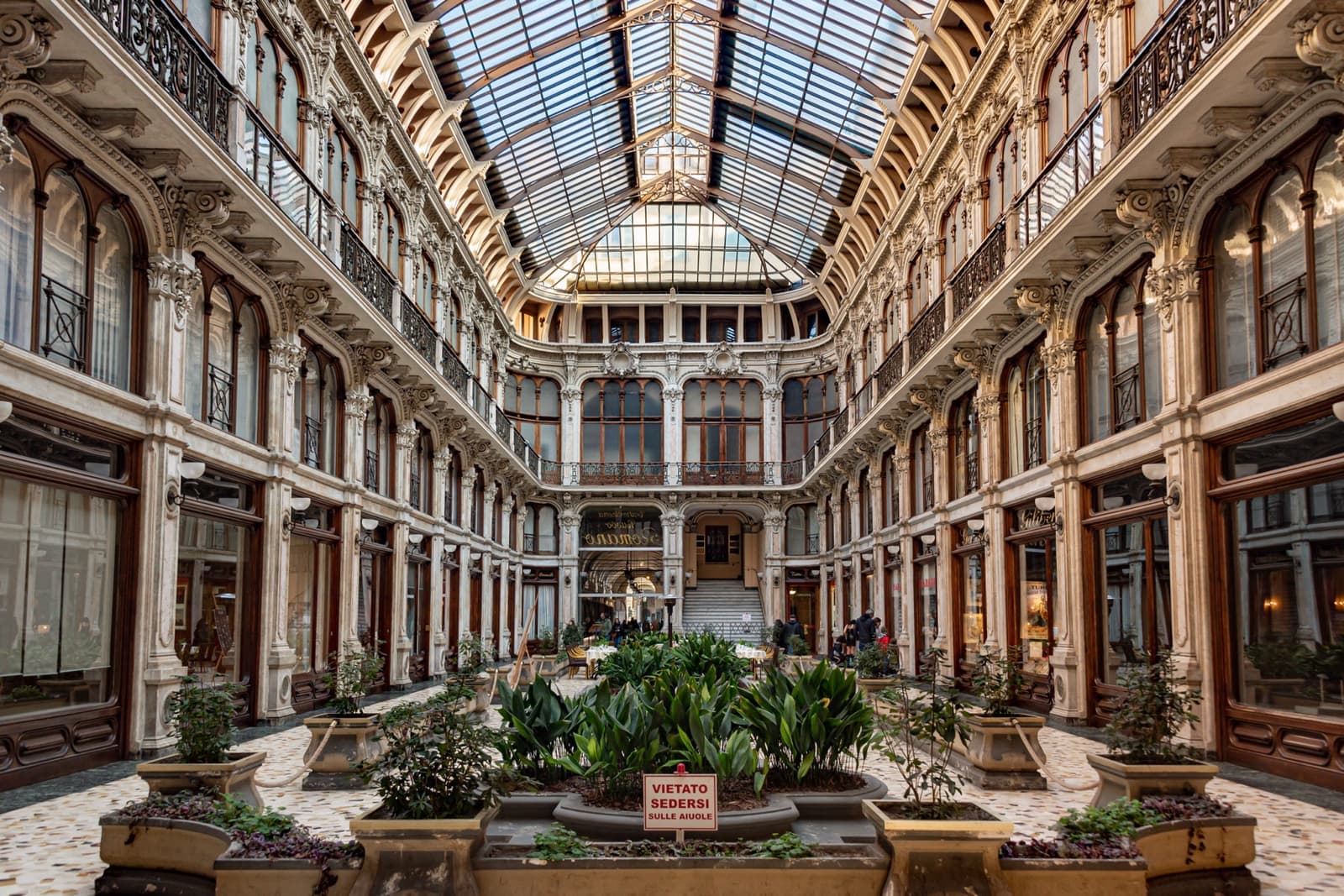 A long shopping arcade with a glass vaulted roof, balconies and potted plants down the middle