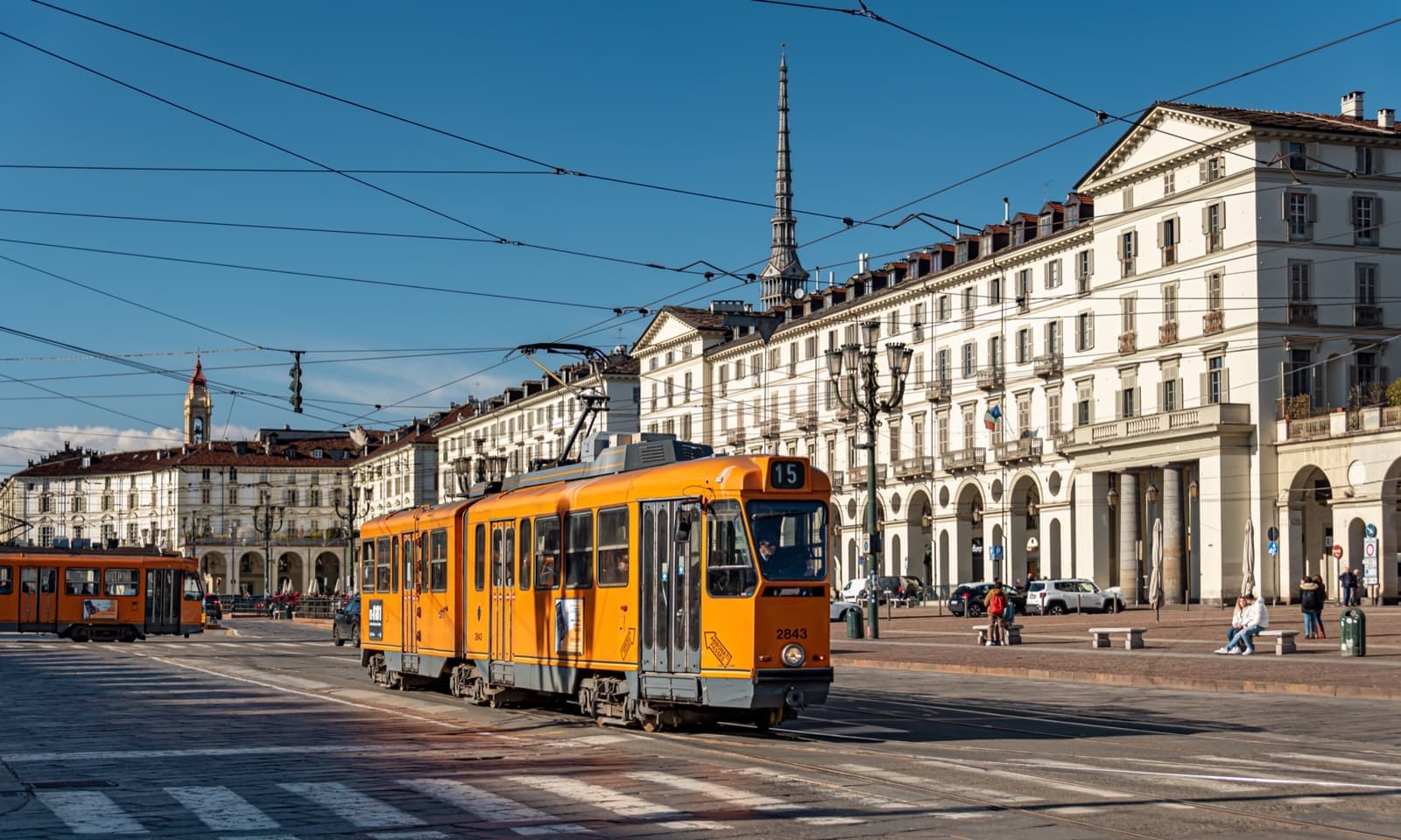 A vast square edged by arcaded buildings, an orange tram crossing in front