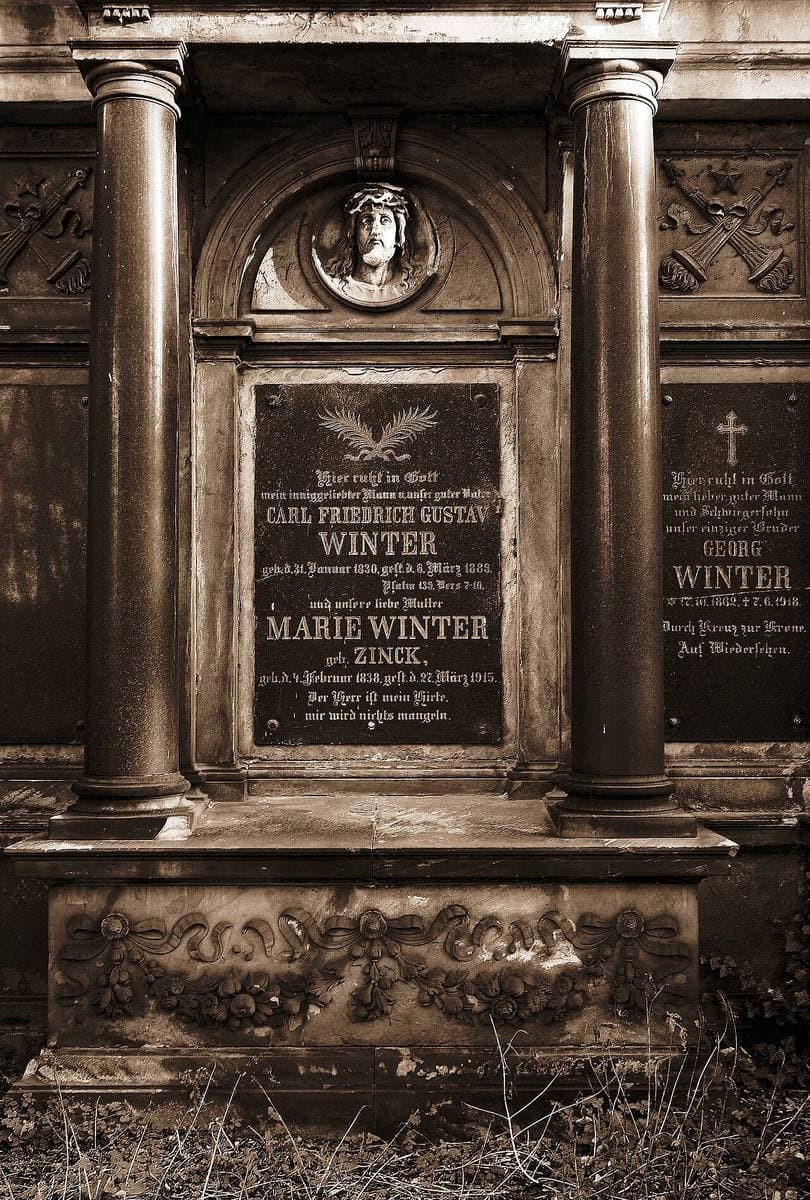 A carved stone wall tomb with columns and black inscription plates