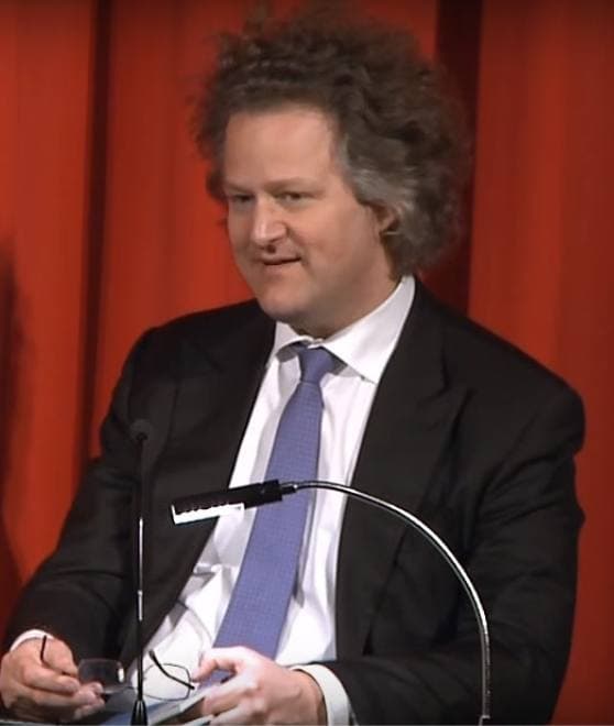 Florian Henckel von Donnersmarck seated at a microphone against a red curtain
