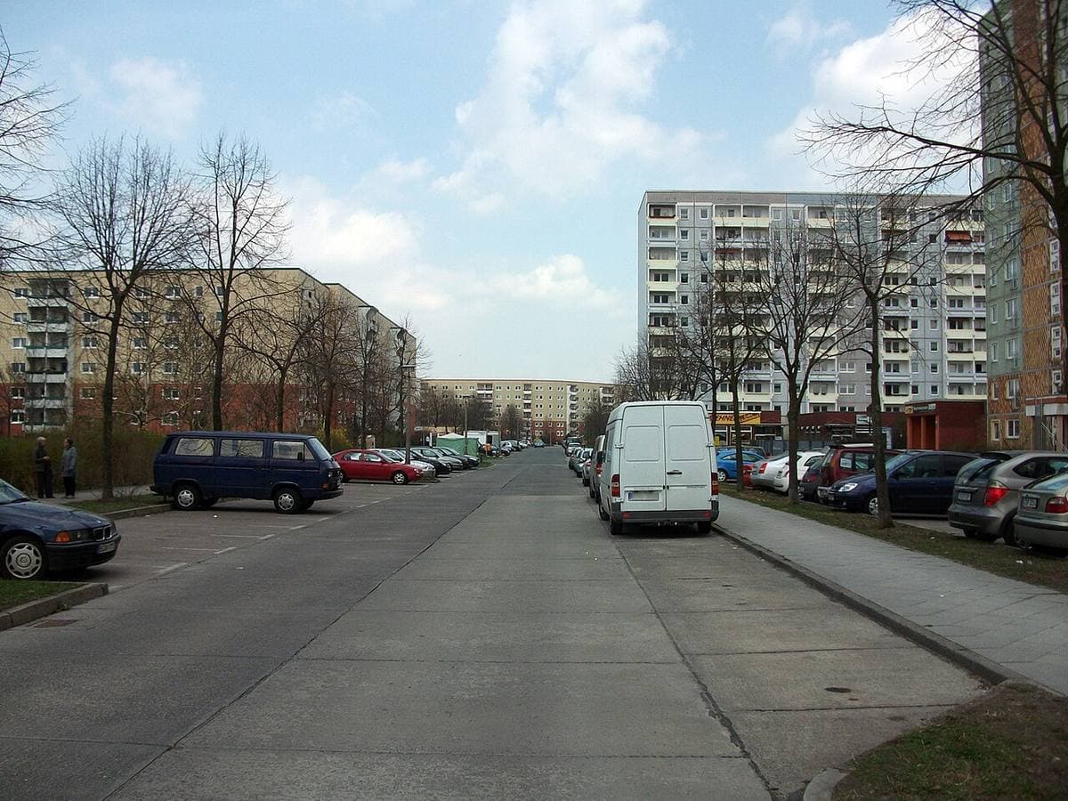 A wide street of parked cars between prefabricated blocks