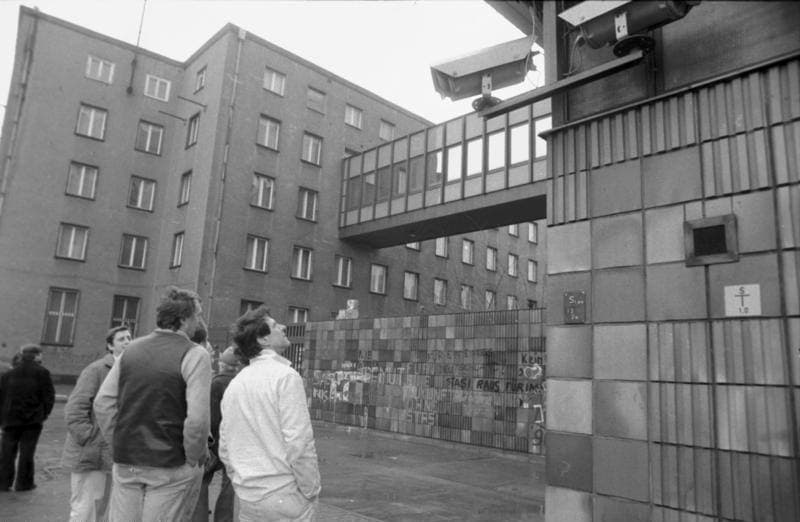 People standing in Ruschestraße below the Stasi office blocks and a covered bridge, January 1990