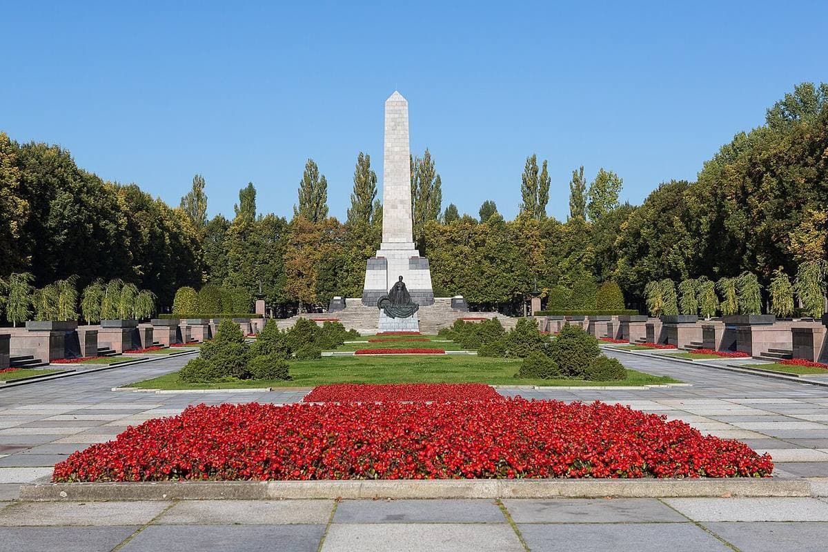 A tall obelisk over red flower beds at the Soviet memorial in Pankow