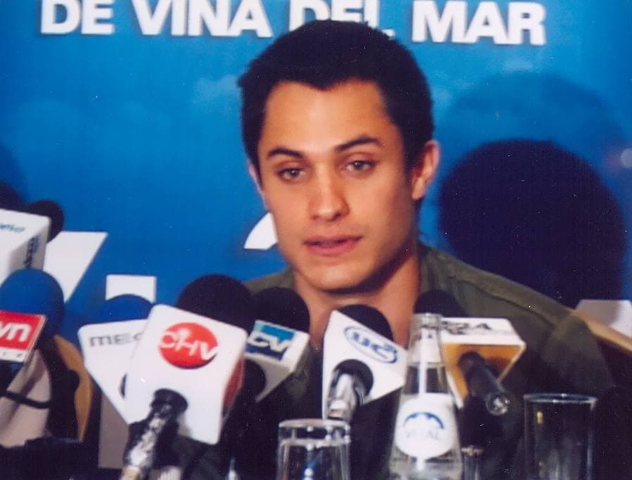 Gael García Bernal at a press table, speaking into a bank of microphones