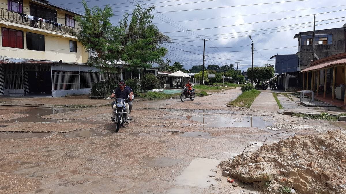 A wet street in Leticia with a motorbike, low houses and power lines