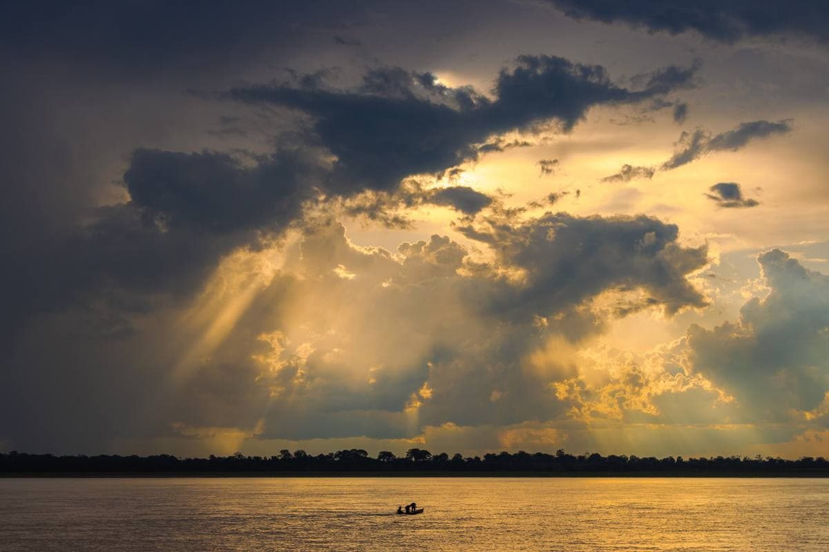 Storm clouds and gold light over the wide Amazon, a small boat on the water