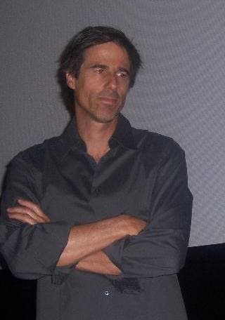 Walter Salles in a dark shirt, arms folded, in front of a cinema screen
