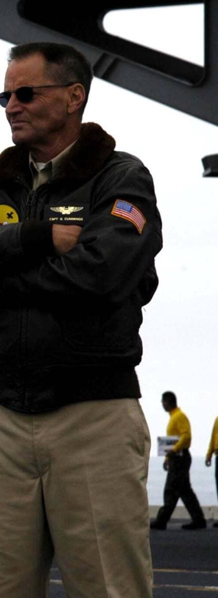 Sam Shepard standing with folded arms on an aircraft carrier deck