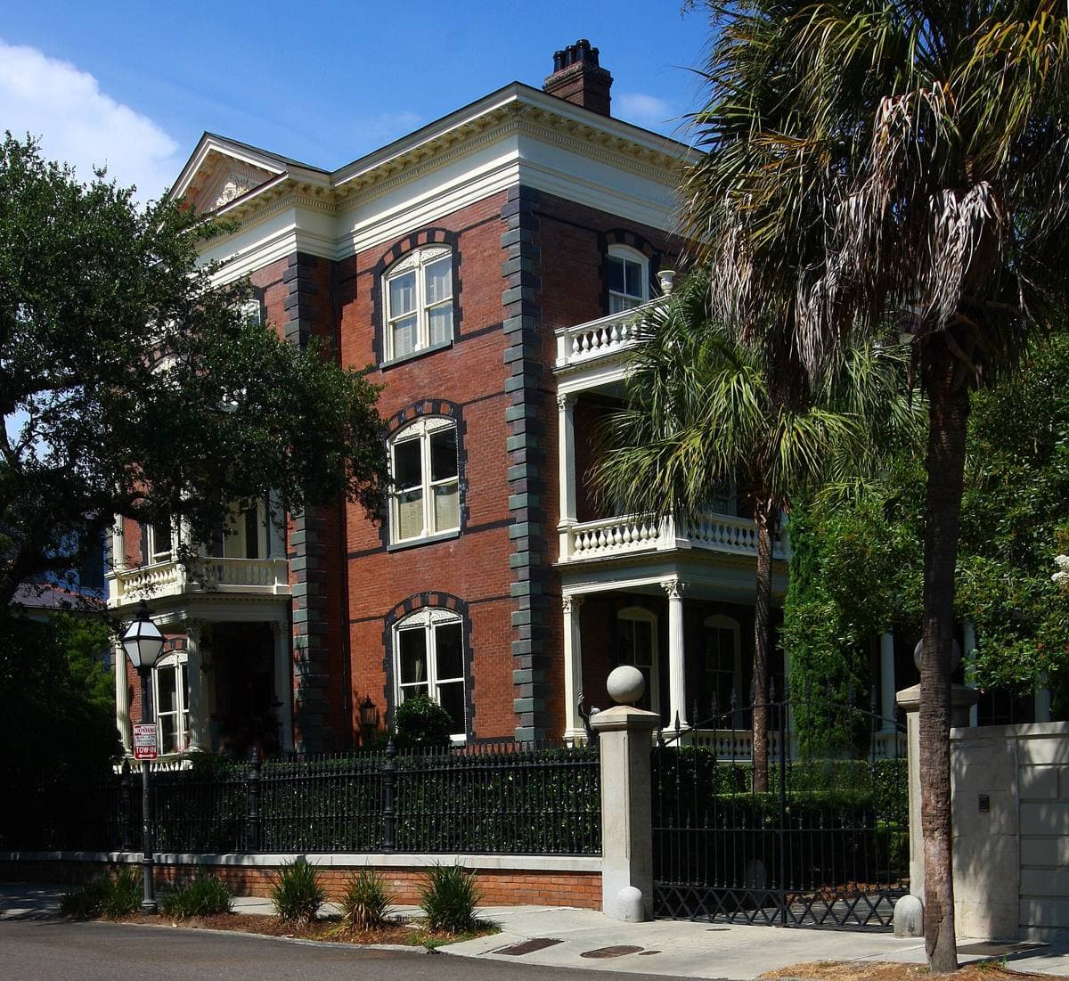 A tall Victorian mansion with a tower and porches behind iron railings