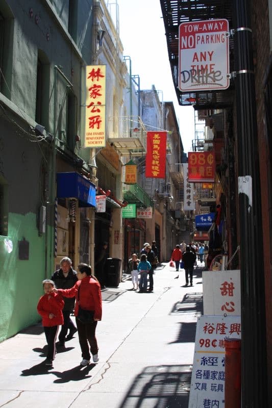 A narrow Chinatown alley with shopfronts and hanging signs