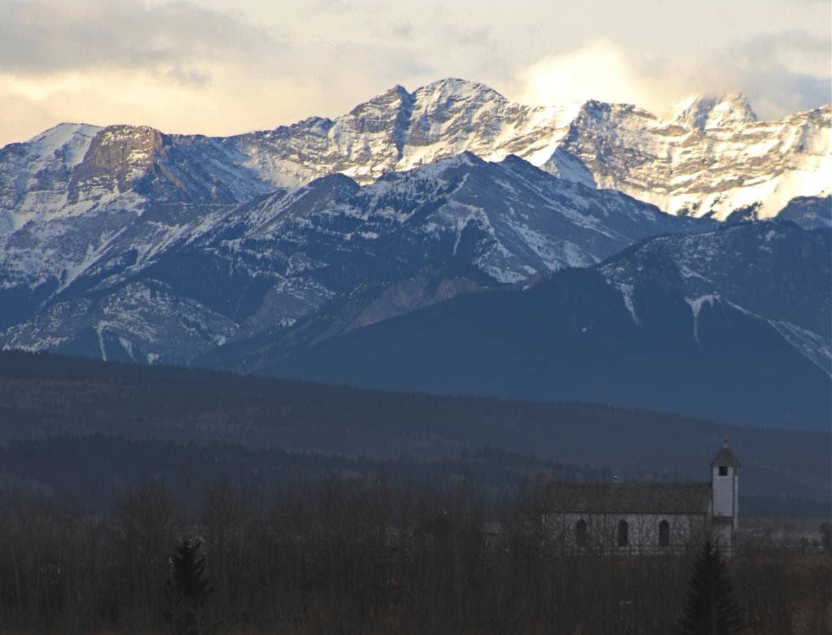 A snowy mountain range with a small white church in the foreground