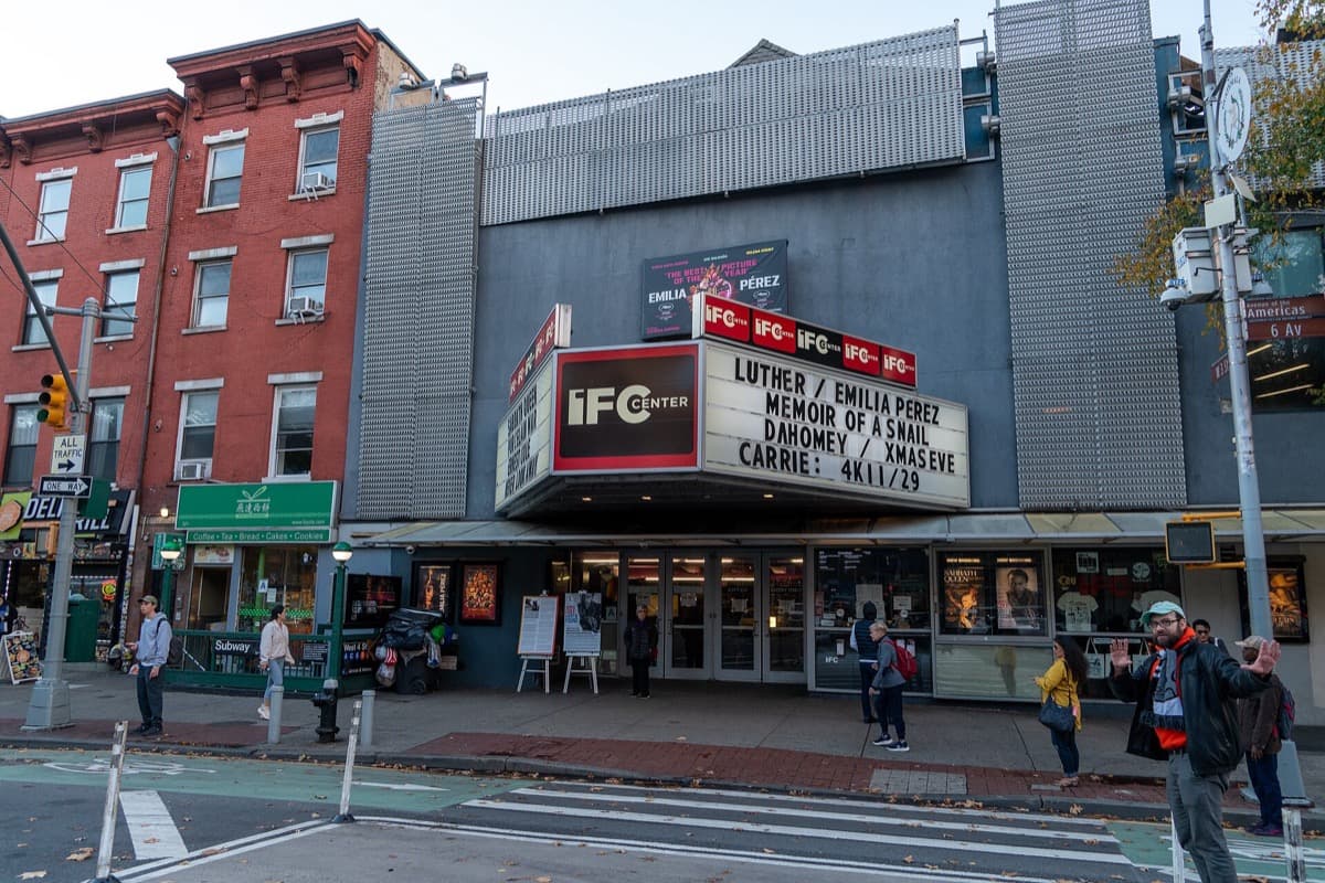 A corner cinema building with a lit marquee on Sixth Avenue, New York