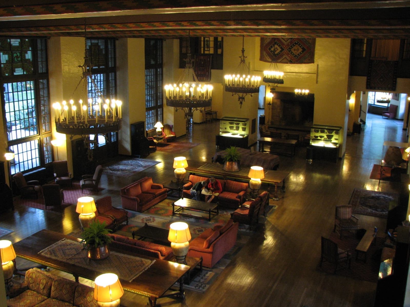 A tall lounge with iron chandeliers, patterned beams and tall windows above sofas