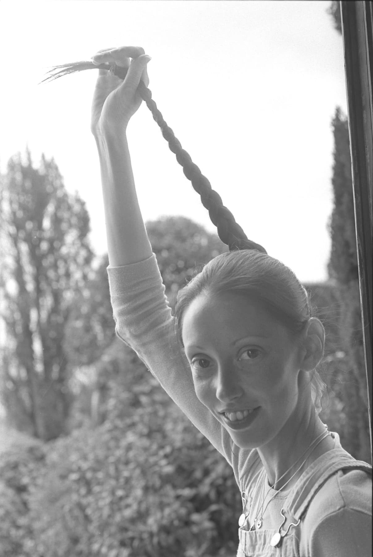 Shelley Duvall smiling at a window, holding her long braid up over her head