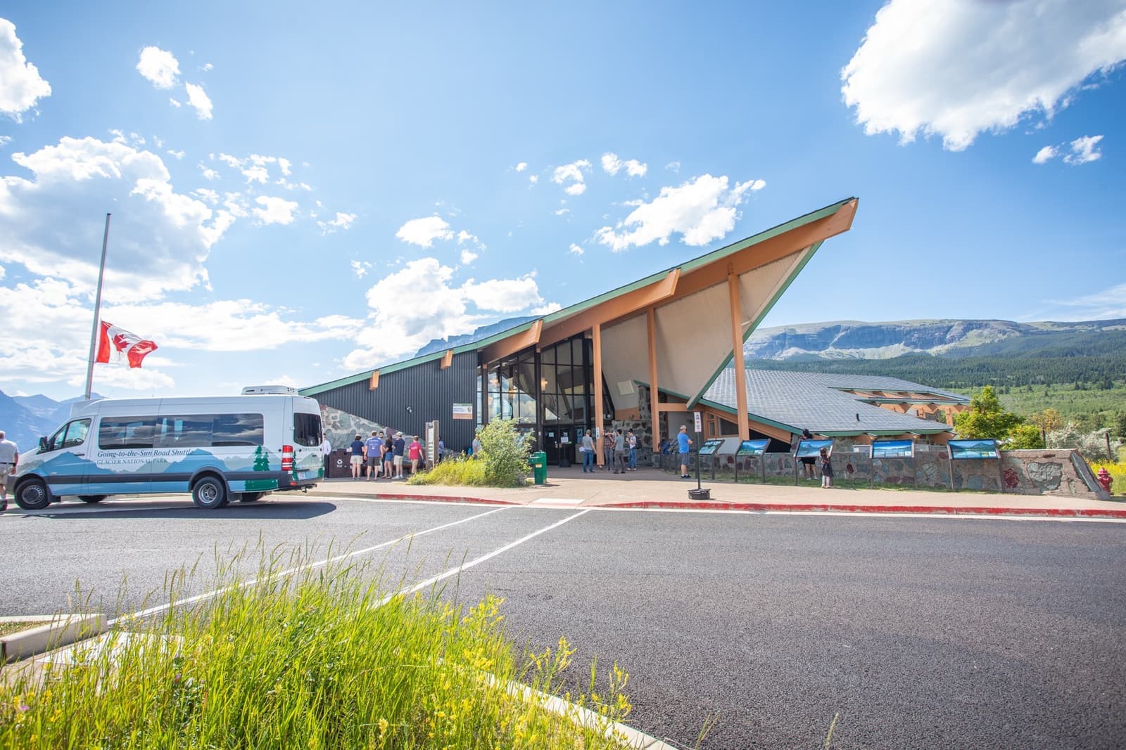 A visitor centre with a steep pointed roof under a blue sky, a shuttle van parked in front and mountains behind
