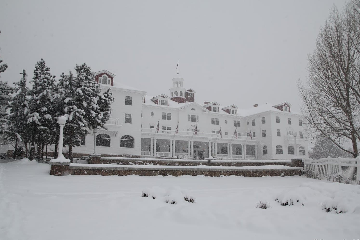 A long white hotel with a red roof and a cupola behind snow-covered lawns