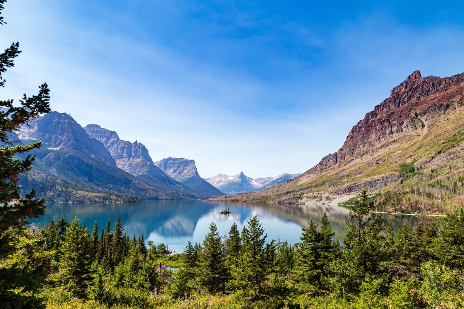 A tiny wooded island in a long turquoise lake between steep mountains