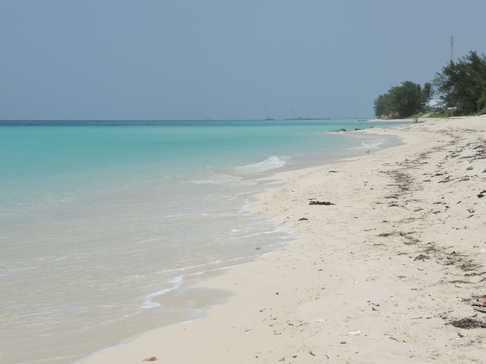Pale sand and clear shallow turquoise water under a hazy sky