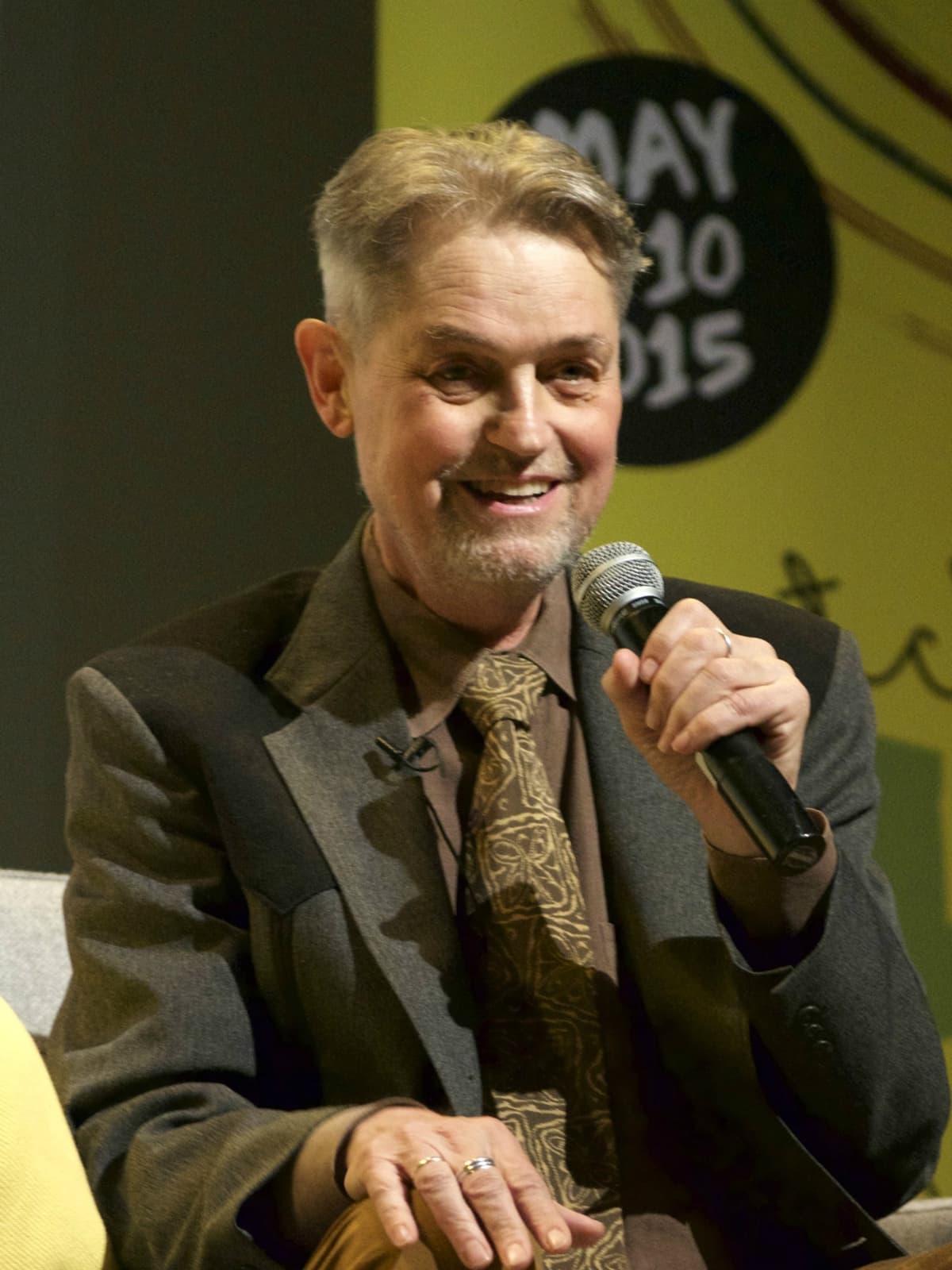Jonathan Demme, grey-haired, in a suit and tie, speaking into a microphone