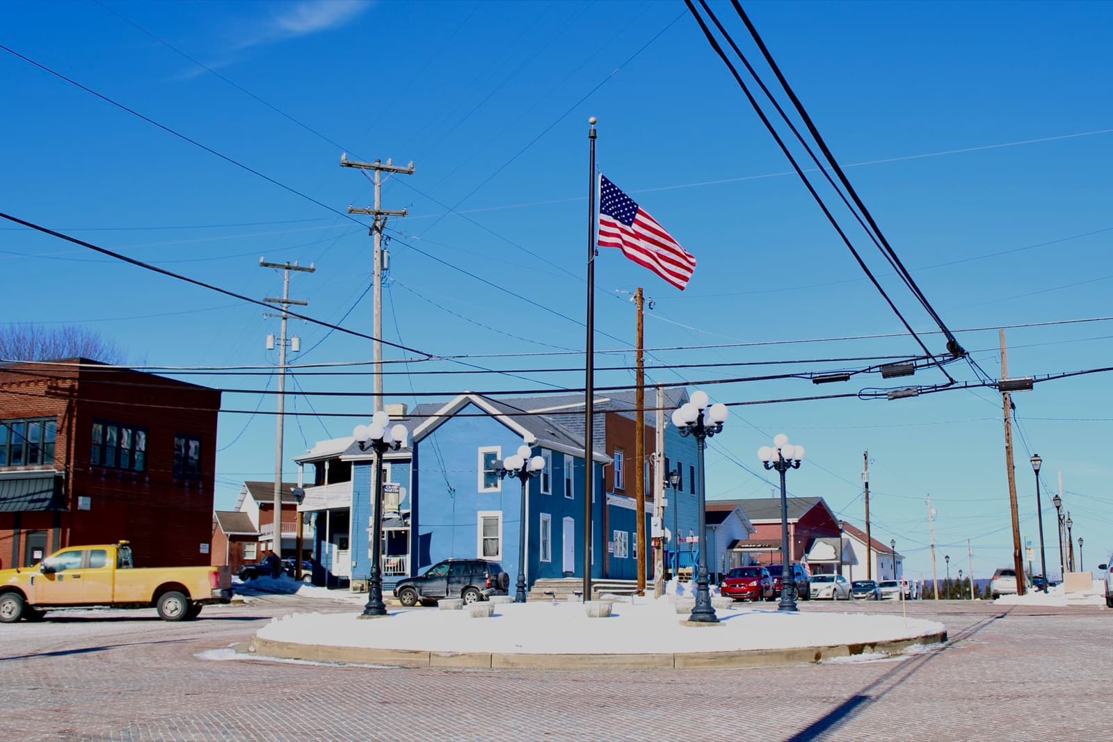 A small-town crossroads with a flagpole, lamp posts and a blue house