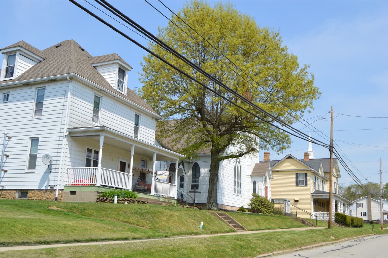 A quiet street of clapboard houses with porches under a spring tree