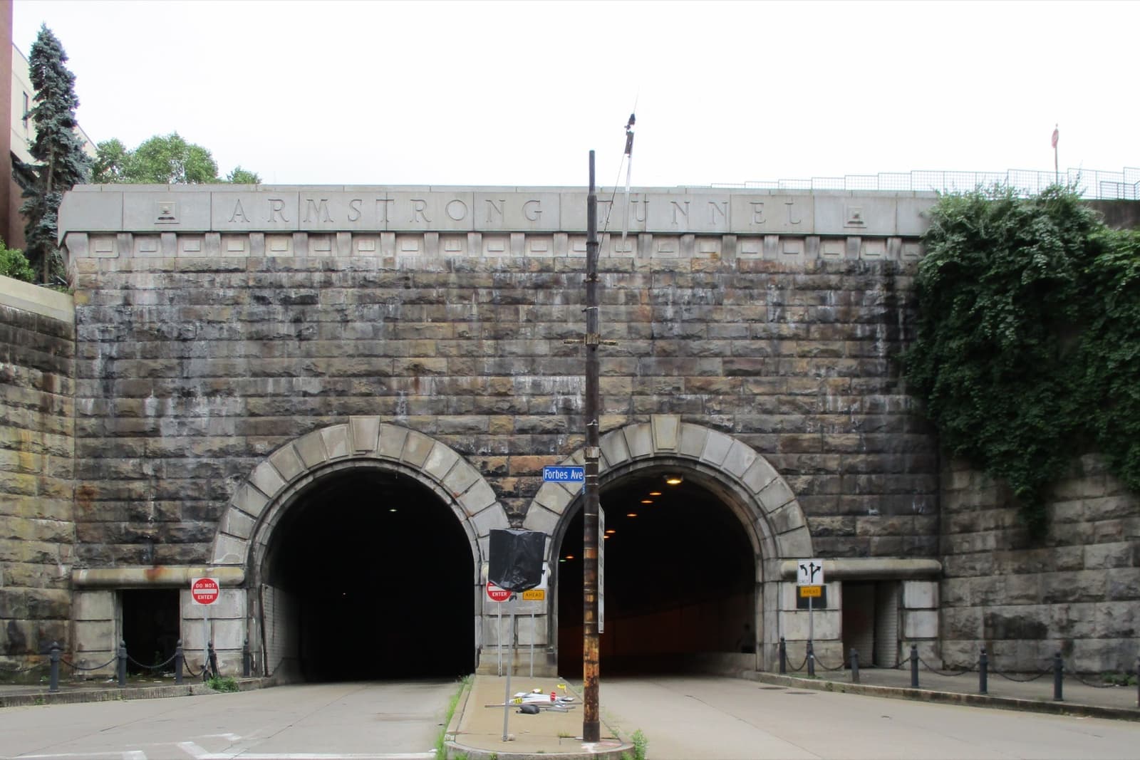 Two arched tunnel mouths in a stone portal below a wooded bluff