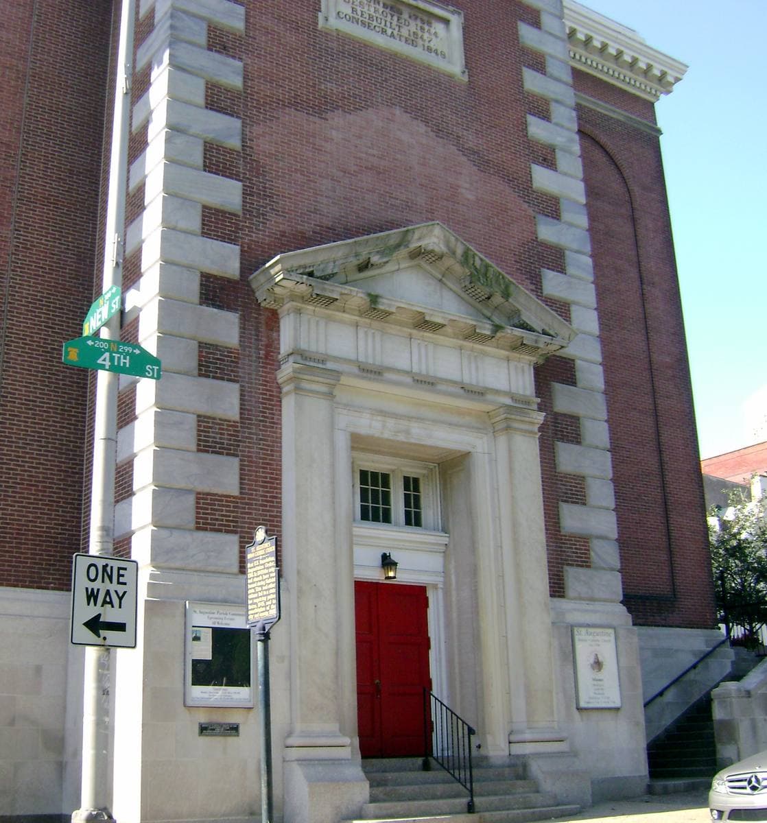 A red door in a pale stone doorcase in the brick side of St Augustine’s church