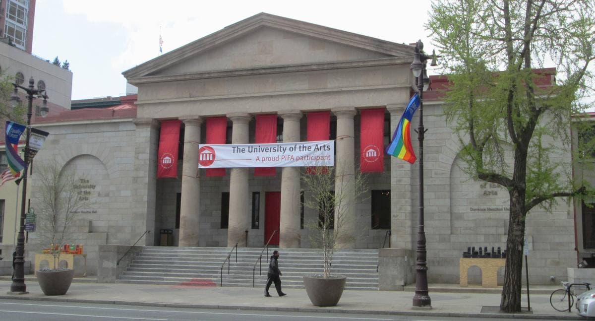 A grey stone hall with columns and red banners at the corner of Broad and Pine