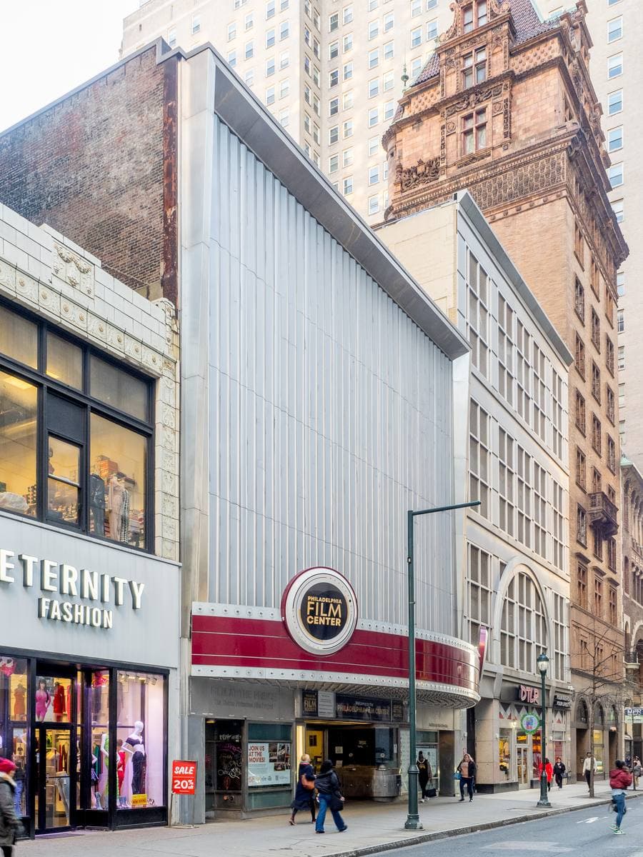 A narrow white theatre front with a round Film Center sign on a busy Chestnut Street block