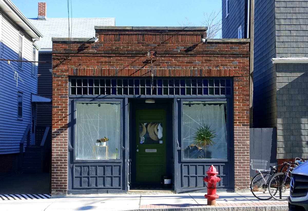 A small brick shopfront with a green door and a red fire hydrant