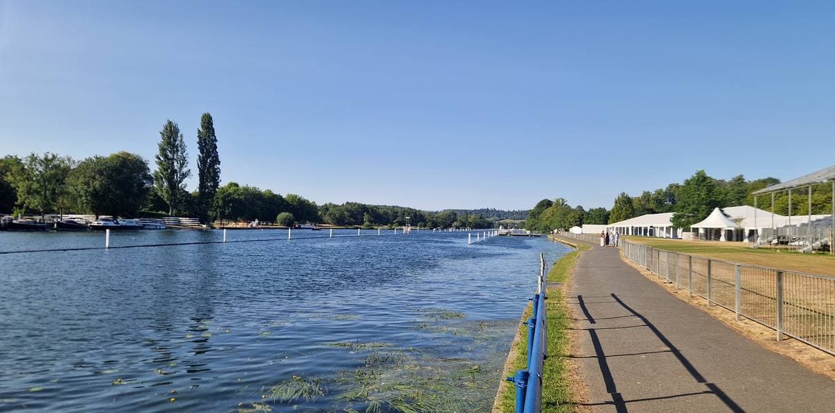 A wide straight reach of the Thames lined with booms and trees