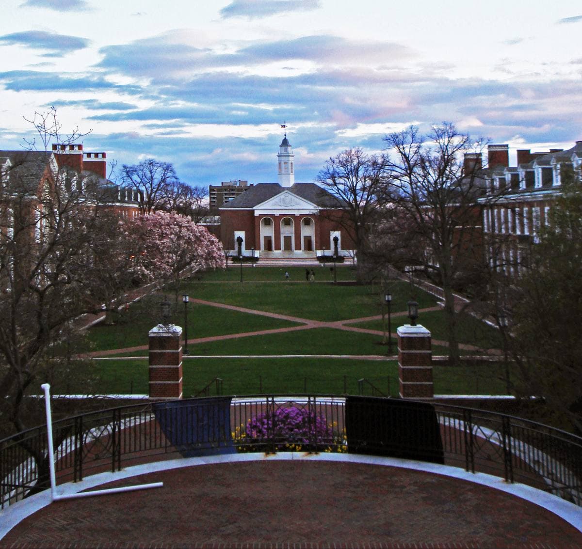 A green campus quad seen from a balustrade, brick buildings and a white cupola beyond