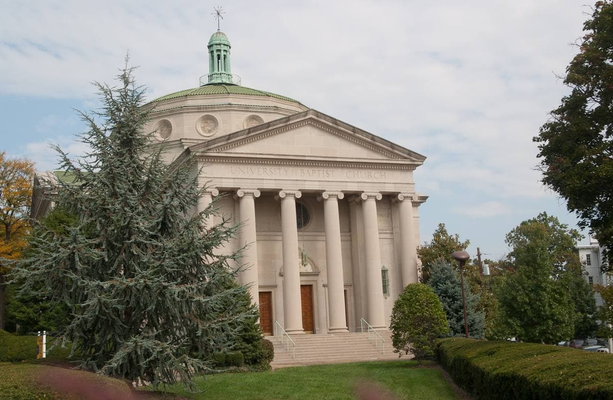 A domed church with a white columned portico behind a cedar tree
