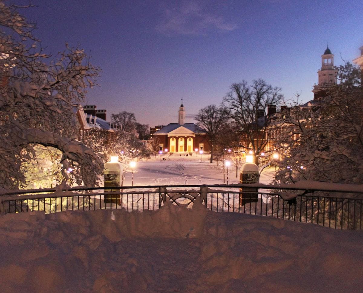 A snowy campus quad at night, lamps glowing, a white-towered brick hall in the distance