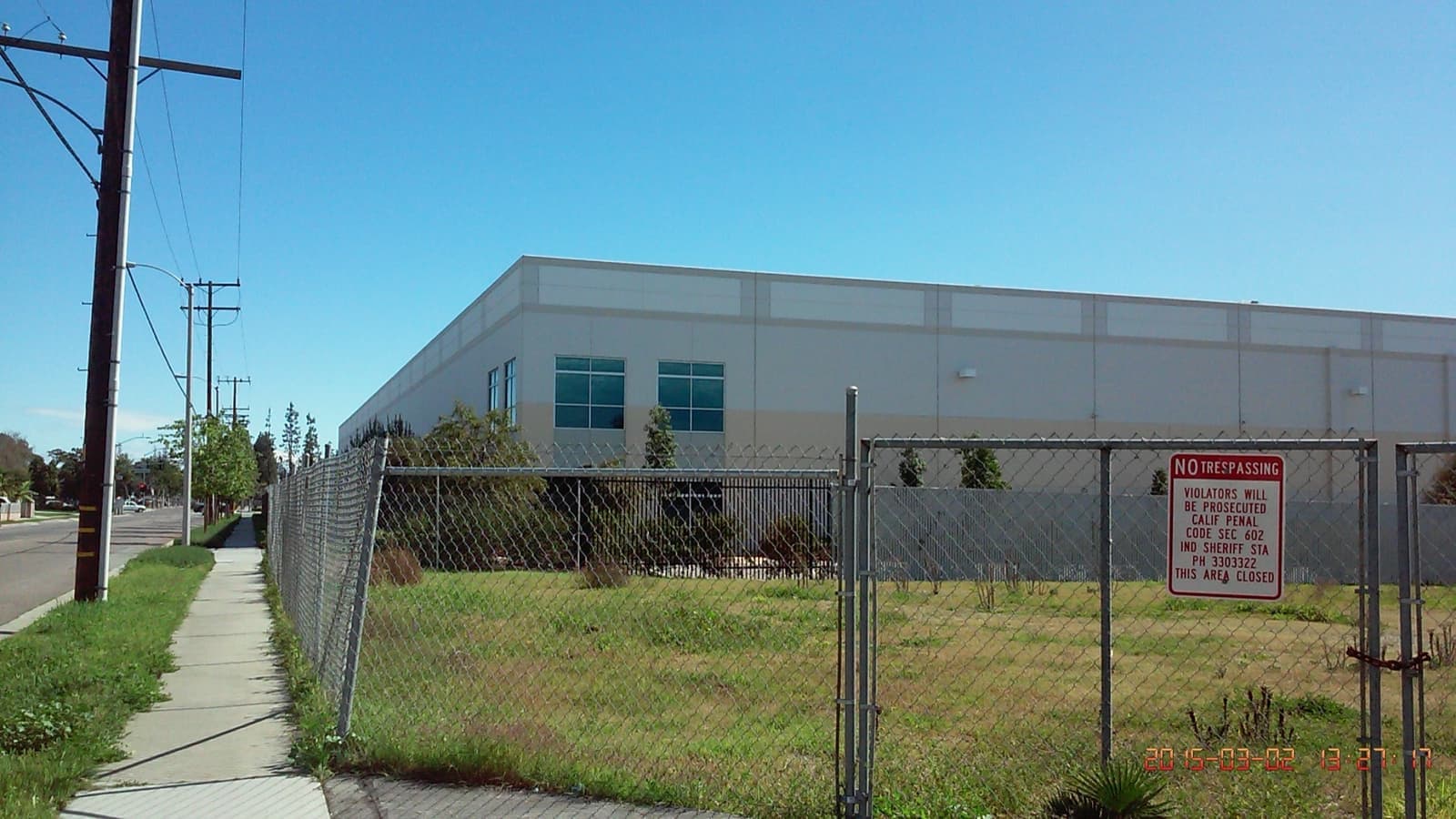 A pale warehouse behind a wire fence