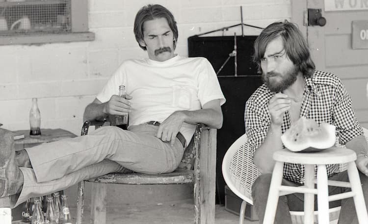 Two men talking beside film equipment on a farmhouse location