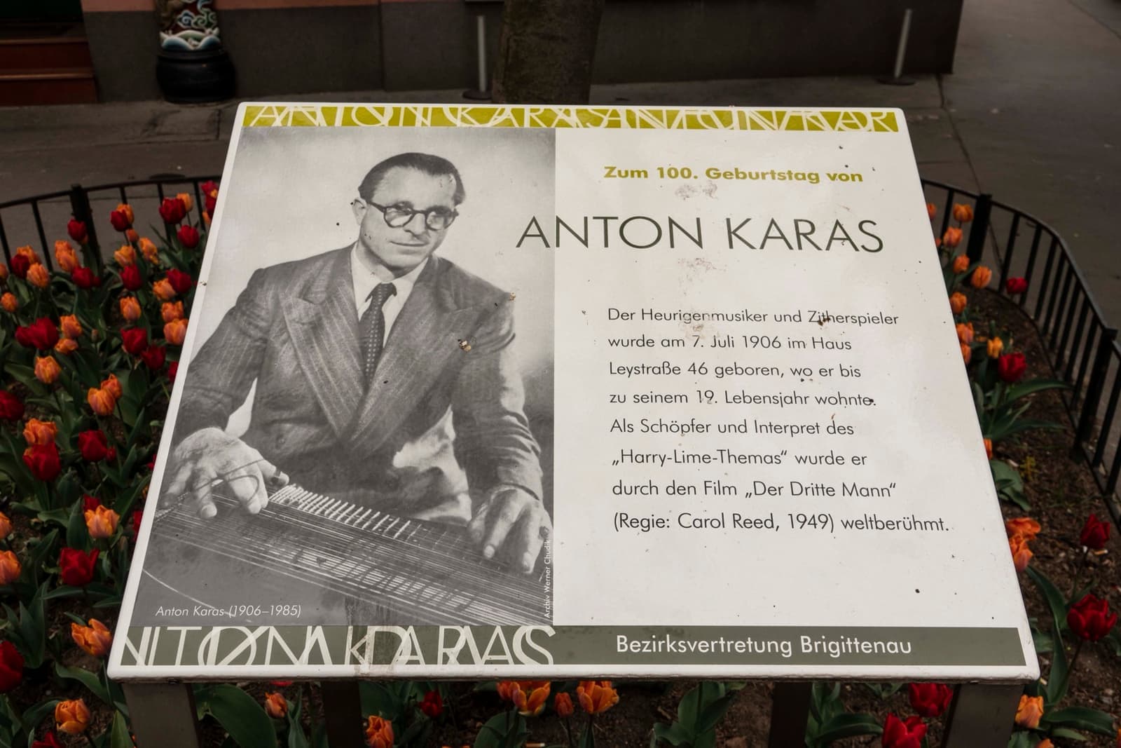 A plaque with a photograph of Anton Karas at his zither, in a flower bed