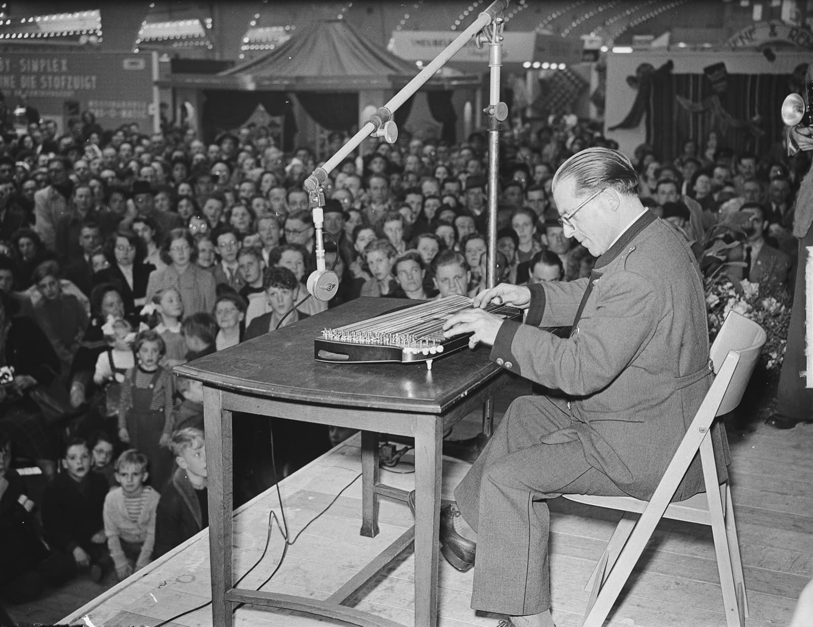 Anton Karas playing a zither on a stage before a large crowd
