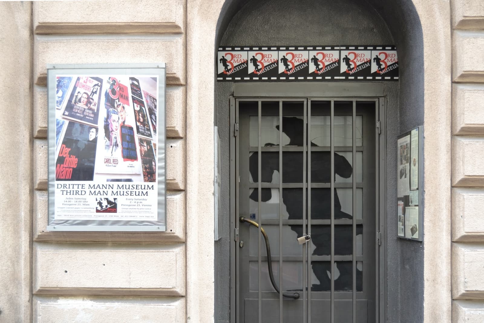 A barred doorway painted with a man’s shadow, beside a museum poster