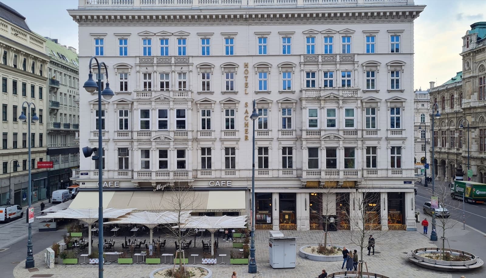 A white hotel front with café awnings on a paved square