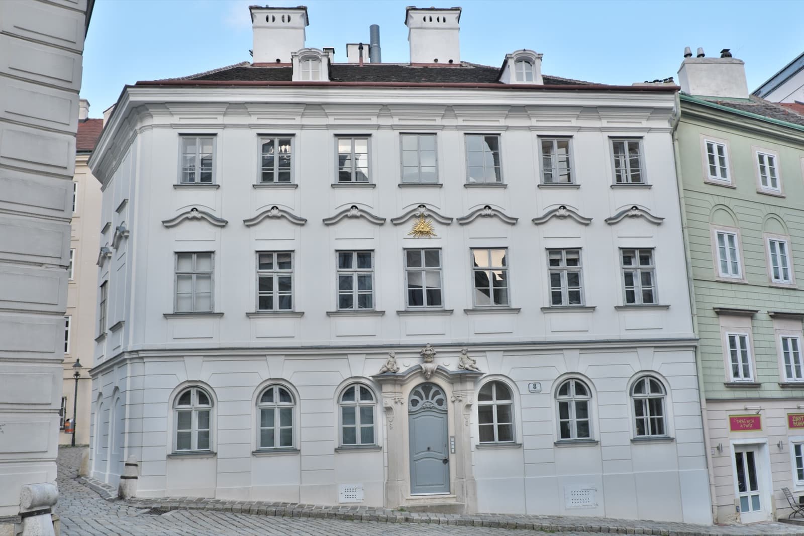 A pale three-storey baroque house with a central arched doorway on a cobbled lane