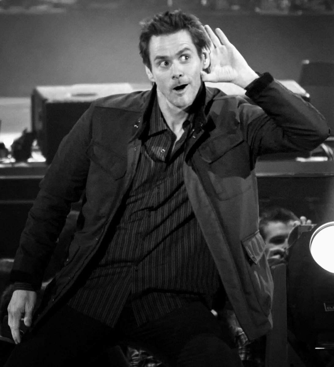 Jim Carrey cups a hand to his ear and pulls a face on stage