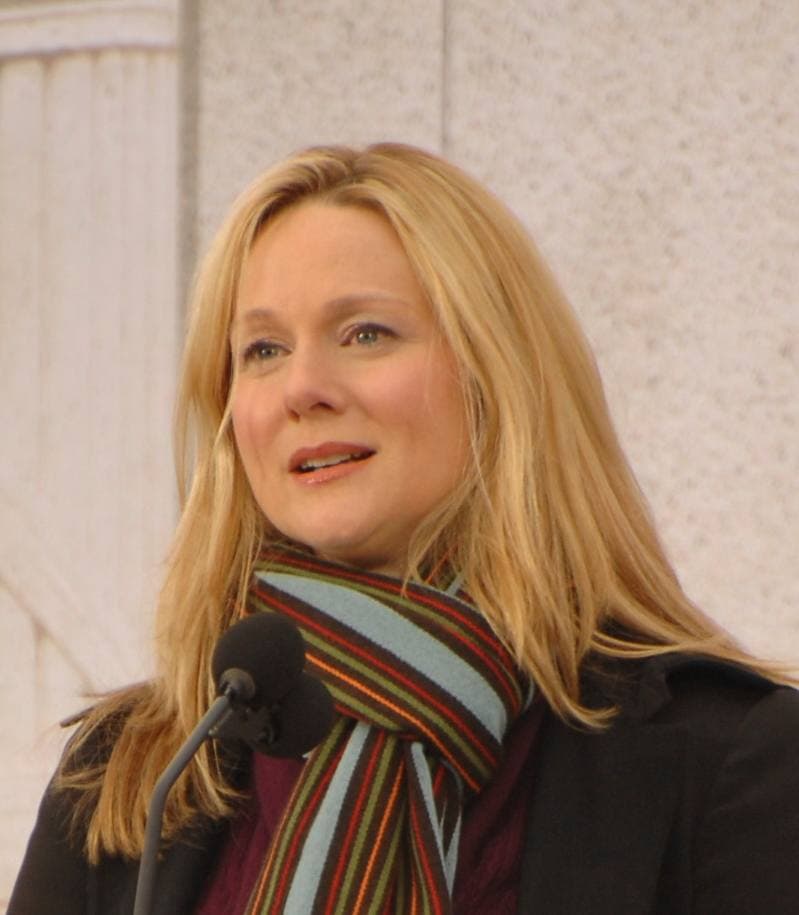 Laura Linney, in a striped scarf, speaks into a microphone outdoors