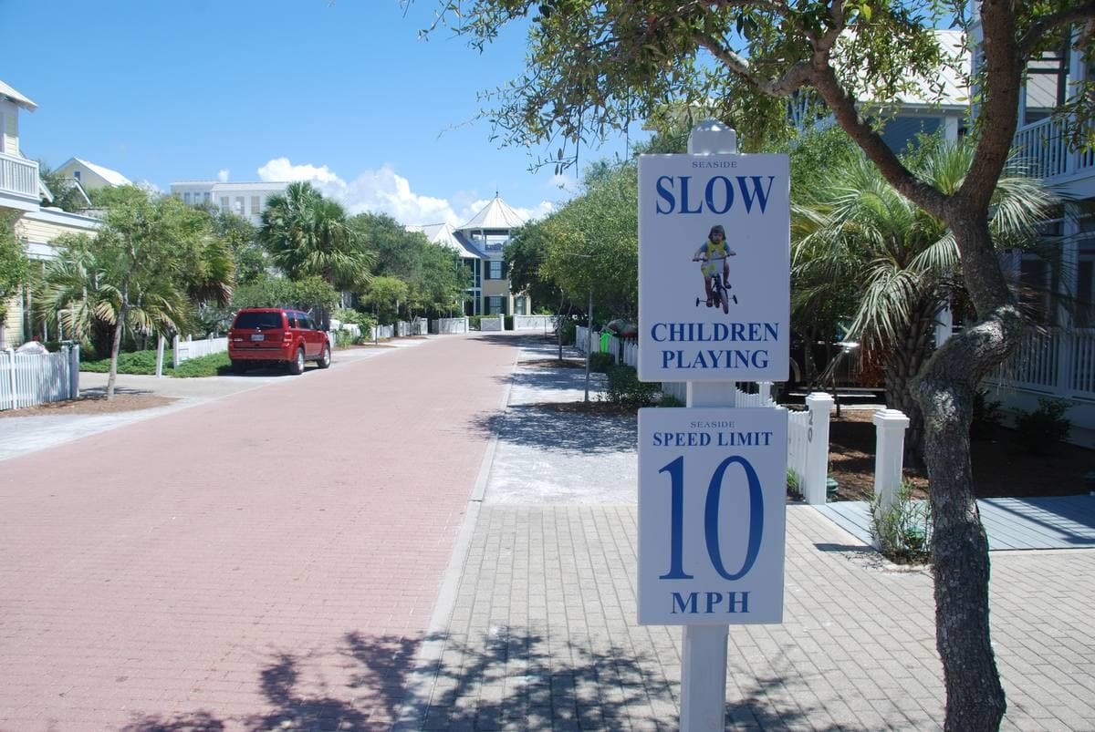 A brick-paved Seaside street lined with palms, porches and a slow sign
