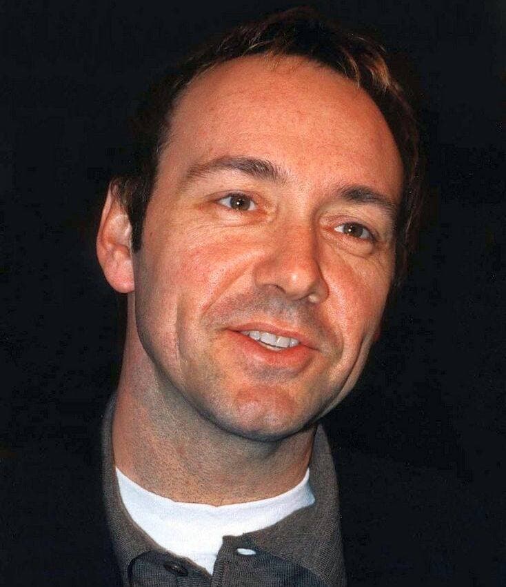 Kevin Spacey smiling, in an open-necked grey shirt