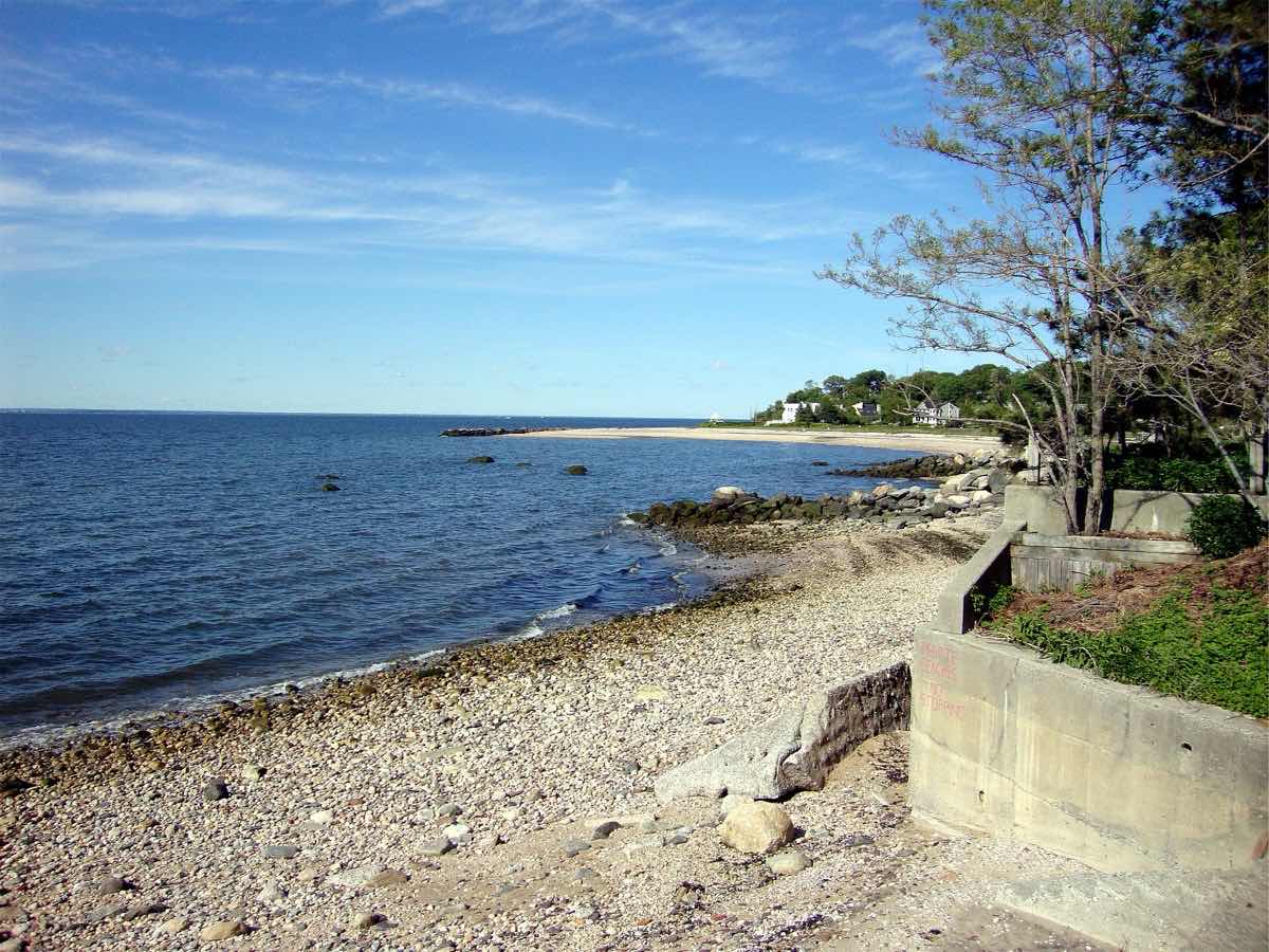 A rocky beach on a calm sound with houses along the shore