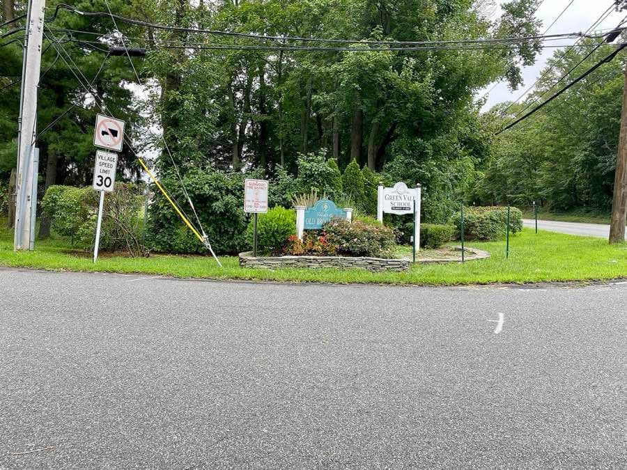 A welcome sign for the village of Old Brookville beside a lane